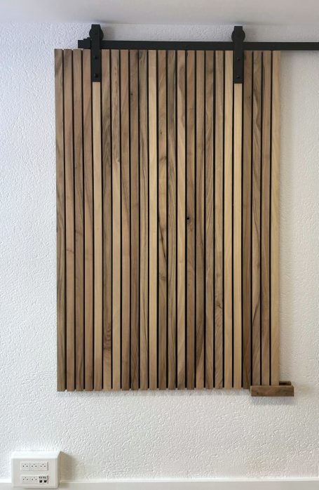 porte coulissante claire voie menuiserie aménagement intérieur guillemot barbezieux cellule commerciale Panneau en bois stratifié aux lignes verticales, suspendu sur un mur.