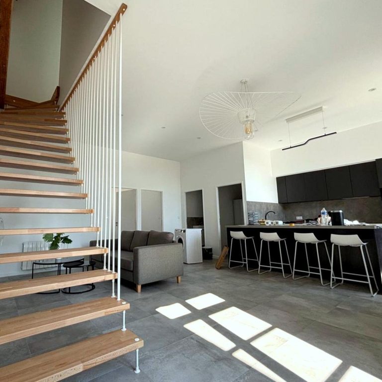 Escalier en bois menant à un espace de vie moderne avec cuisine ouverte.